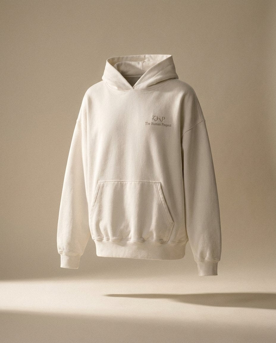 The In Progress hoodie in bone, floating in warm light