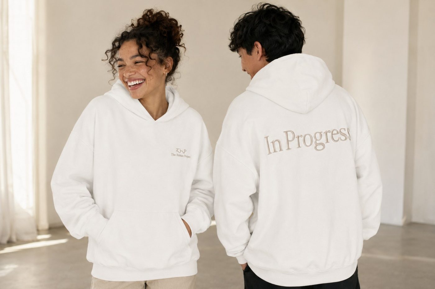 Two people laughing in the bone hoodies, one showing the In Progress back